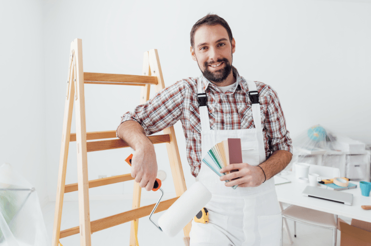 Confident professional painter posing, he is holding a paint roller and color swatches, home renovation and decoration concept